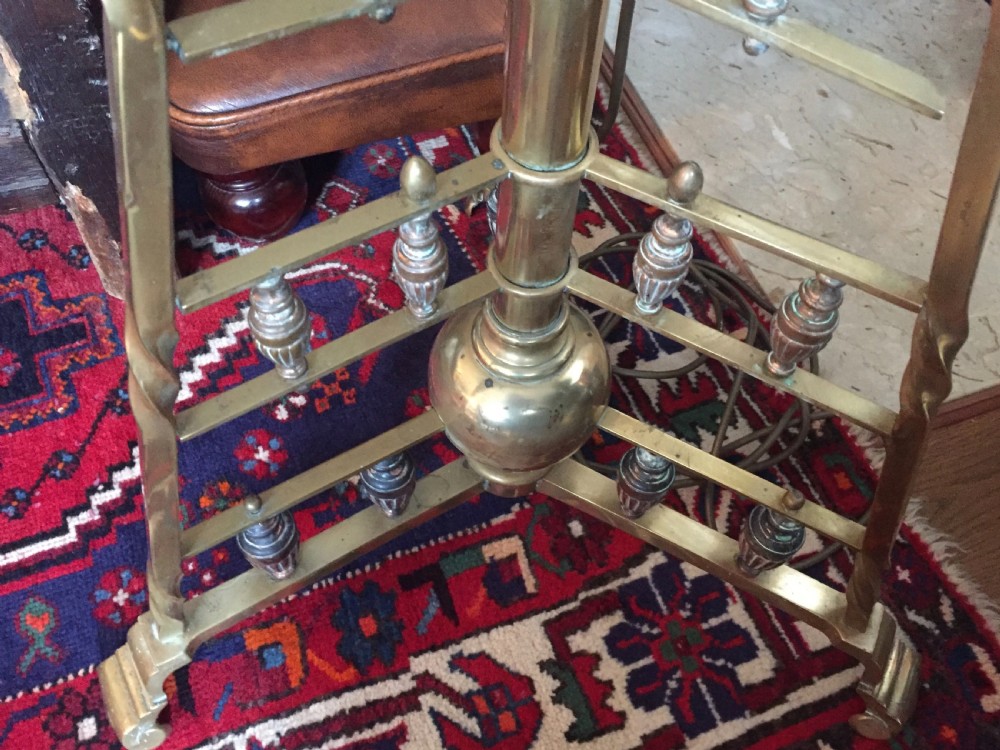 An Arts and Crafts brass standard lamp featuring a telescopic central column supported by a stepped triangular tripod base with turned finials. View XII