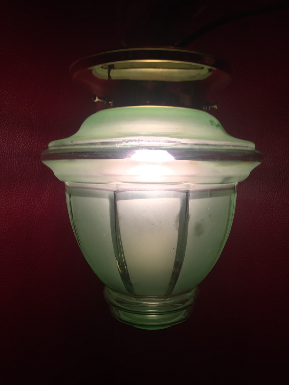 An illuminated Art Deco ceiling globe made of green frosted glass with ribbed panel details.