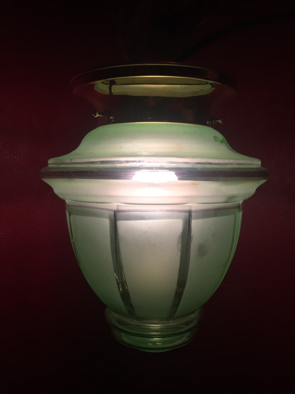 An illuminated Art Deco ceiling globe made of green frosted glass with ribbed panel details. View III