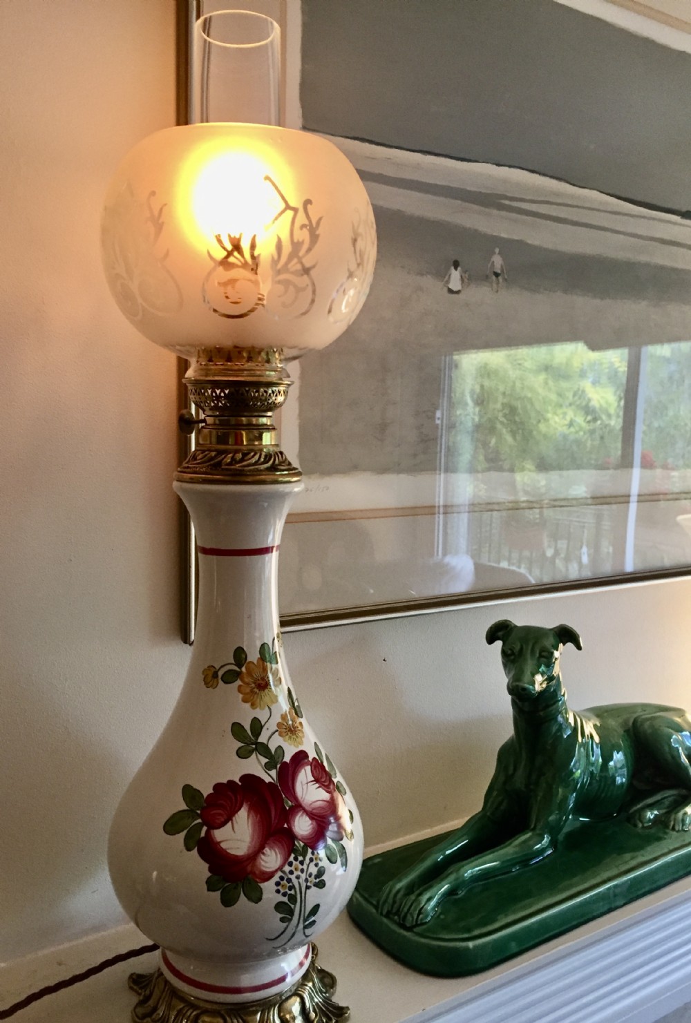 A 19th-century French faience oil lamp with hand-painted floral motifs on a cream body, set on a cast bronze base with a frosted glass globe.