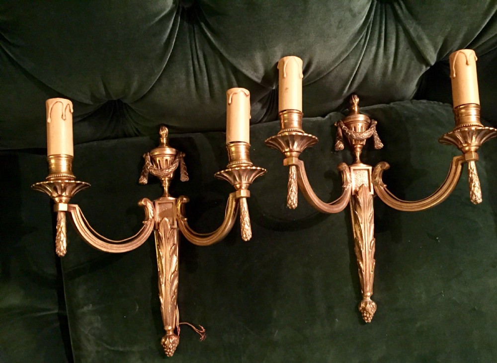 A pair of nineteenth-century French Napoleon III gilt bronze two-arm wall sconces featuring classical urn finials, drapery swags, and acanthus leaf detailing.