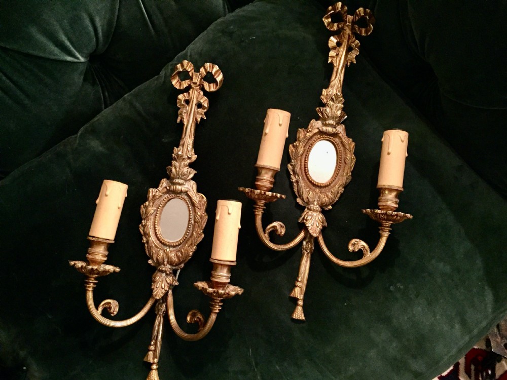 A pair of French Napoleon III gilt bronze wall girandoles featuring ribbon bow cresting, small oval mirrors, and twin scrolled candle arms with tassel drops. View II
