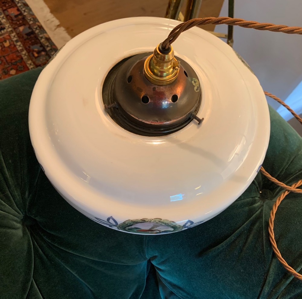 A white glass ceiling pendant shade with a brass top gallery, decorated with hand-painted blue ribbons and a central medallion depicting a cottage. View II
