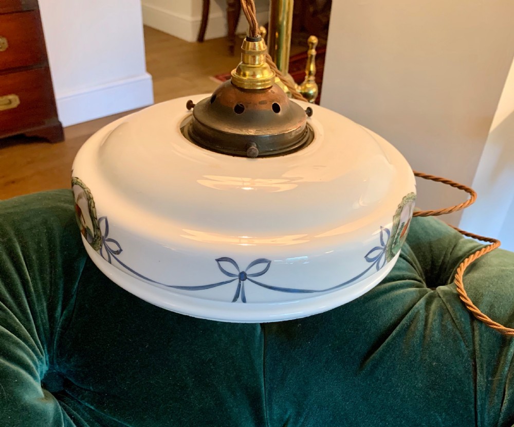 A white glass ceiling pendant shade with a brass top gallery, decorated with hand-painted blue ribbons and a central medallion depicting a cottage. View III