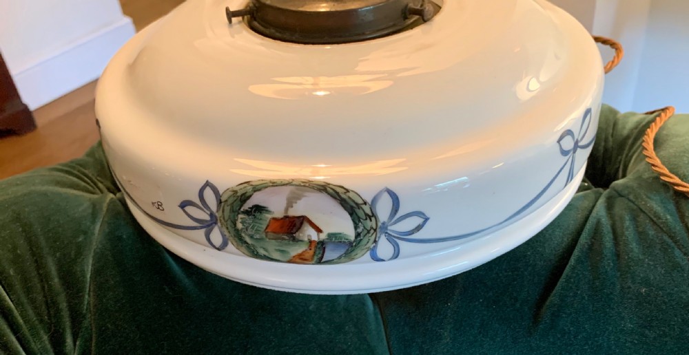 A white glass ceiling pendant shade with a brass top gallery, decorated with hand-painted blue ribbons and a central medallion depicting a cottage. View IV
