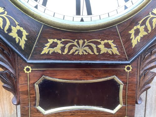 fig 1. An octagonal rosewood drop dial wall clock featuring brass foliage inlay around a cream Roman numeral dial.