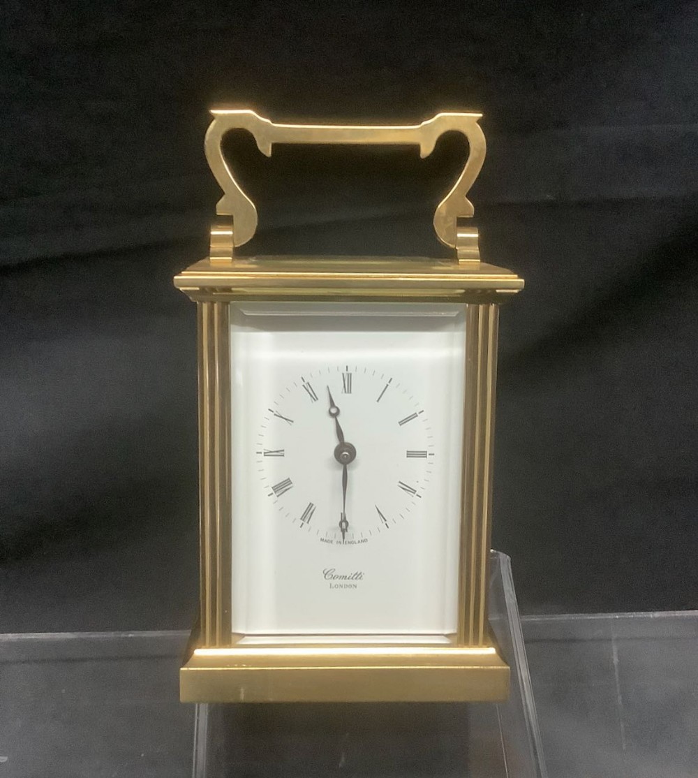 A brass carriage clock with a top carrying handle and a white dial displaying Roman numerals.