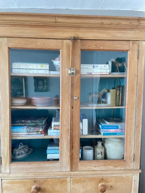 fig 1. A Victorian waxed pine glazed bookcase featuring two upper glass cabinet doors with a blue painted interior over a chest of four drawers with turned knobs.