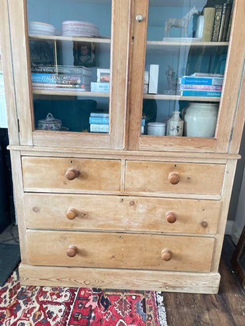 fig 2. A Victorian waxed pine glazed bookcase featuring two upper glass cabinet doors with a blue painted interior over a chest of four drawers with turned knobs.