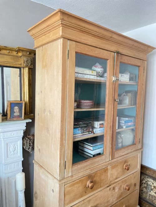 fig 3. A Victorian waxed pine glazed bookcase featuring two upper glass cabinet doors with a blue painted interior over a chest of four drawers with turned knobs.