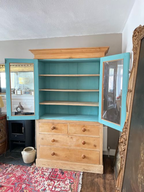 fig 6. A Victorian waxed pine glazed bookcase featuring two upper glass cabinet doors with a blue painted interior over a chest of four drawers with turned knobs.