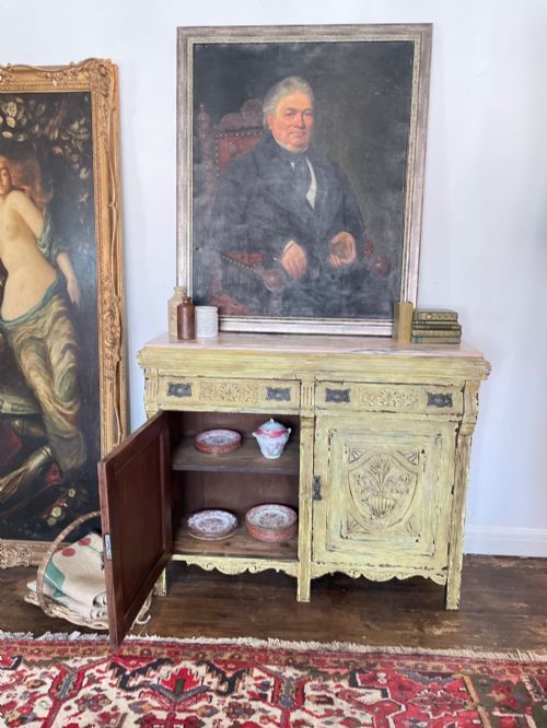 fig 1. An antique French provincial sideboard featuring distressed yellow painted wood, two carved panel doors with urn motifs, two upper drawers, and a pink marble top surface.