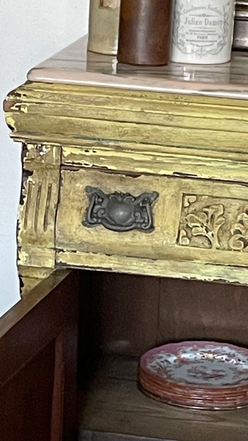 fig 2. An antique French provincial sideboard featuring distressed yellow painted wood, two carved panel doors with urn motifs, two upper drawers, and a pink marble top surface.