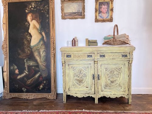 fig 6. An antique French provincial sideboard featuring distressed yellow painted wood, two carved panel doors with urn motifs, two upper drawers, and a pink marble top surface.