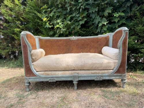 fig 1. A French Louis XVI style daybed featuring a grey-painted curved timber frame with woven cane panels, fitted with a cream linen mattress cushion and two bolster pillows.