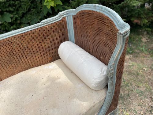 fig 3. A French Louis XVI style daybed featuring a grey-painted curved timber frame with woven cane panels, fitted with a cream linen mattress cushion and two bolster pillows.