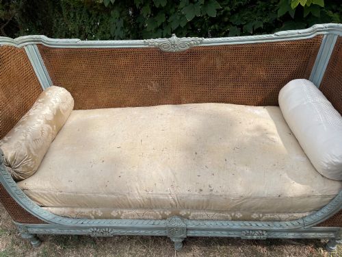 fig 4. A French Louis XVI style daybed featuring a grey-painted curved timber frame with woven cane panels, fitted with a cream linen mattress cushion and two bolster pillows.