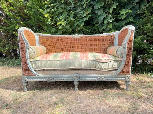 fig 6. A French Louis XVI style daybed featuring a grey-painted curved timber frame with woven cane panels, fitted with a cream linen mattress cushion and two bolster pillows.