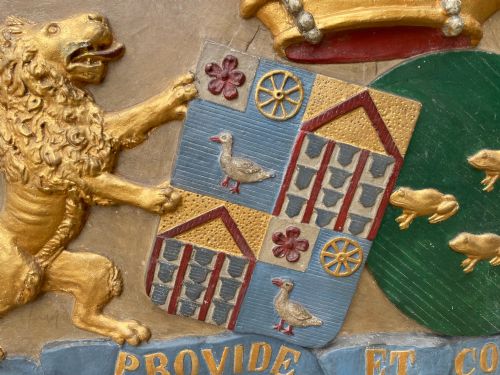 fig 2. A framed 19th-century Dutch heraldic marriage plaque depicting two carved gilt lion supporters holding alliance coats of arms under a helmet crest and motto banner.