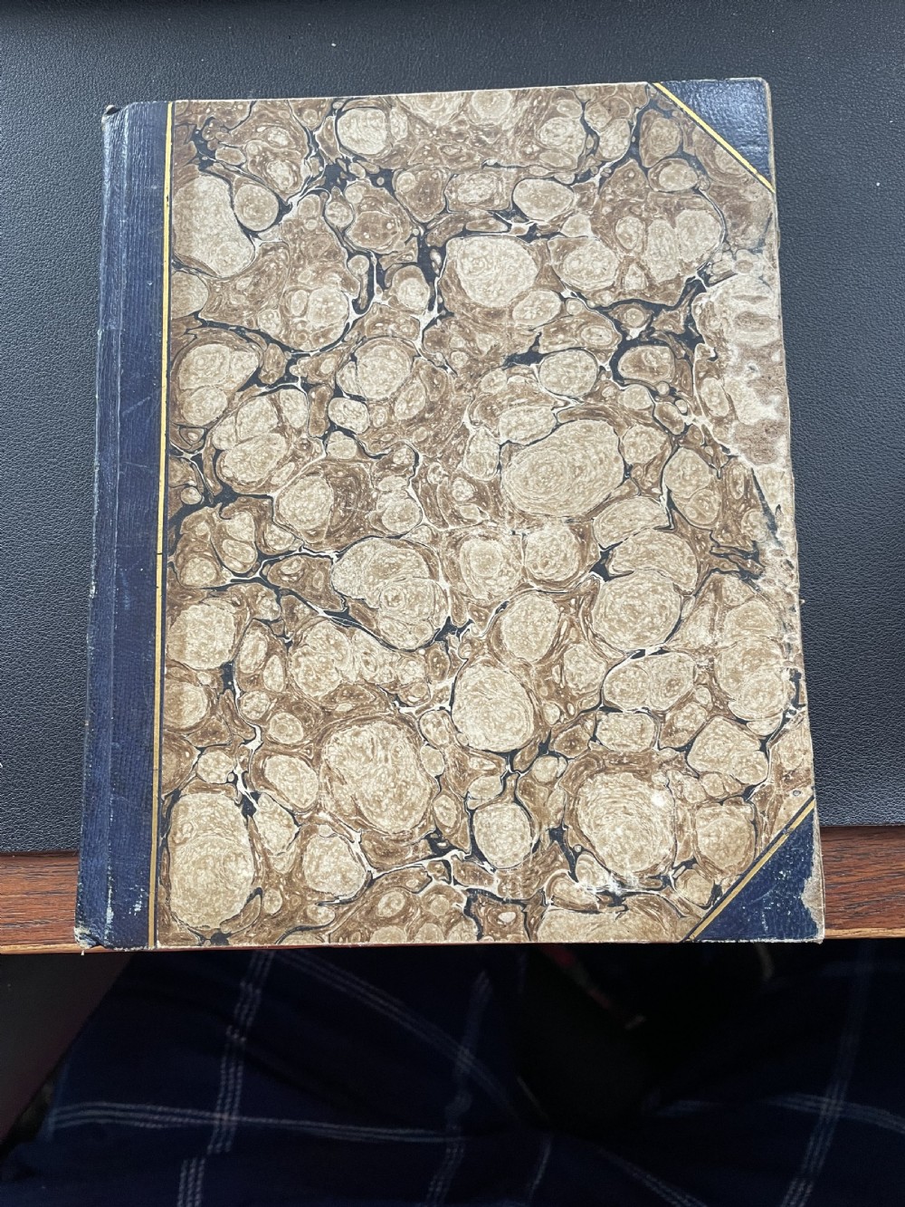 An antique book with dark blue quarter leather binding, gold tooling lines, and brown marbled paper boards.