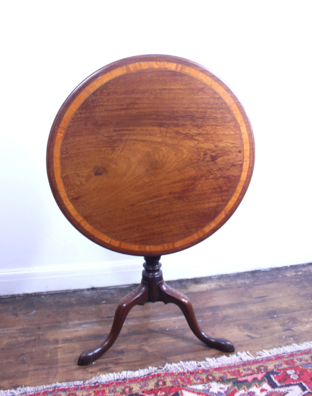 An 18th-century George III mahogany tilt-top tripod table with a circular crossbanded top tilted vertically on a turned stem and splayed legs.