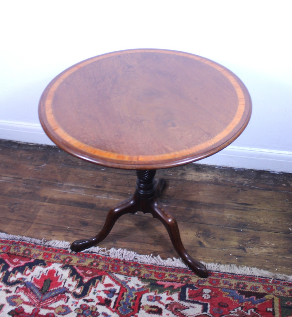 An 18th-century George III mahogany tilt-top tripod table with a circular crossbanded top tilted vertically on a turned stem and splayed legs. View VI
