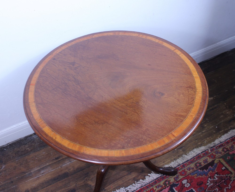 An 18th-century George III mahogany tilt-top tripod table with a circular crossbanded top tilted vertically on a turned stem and splayed legs. View X