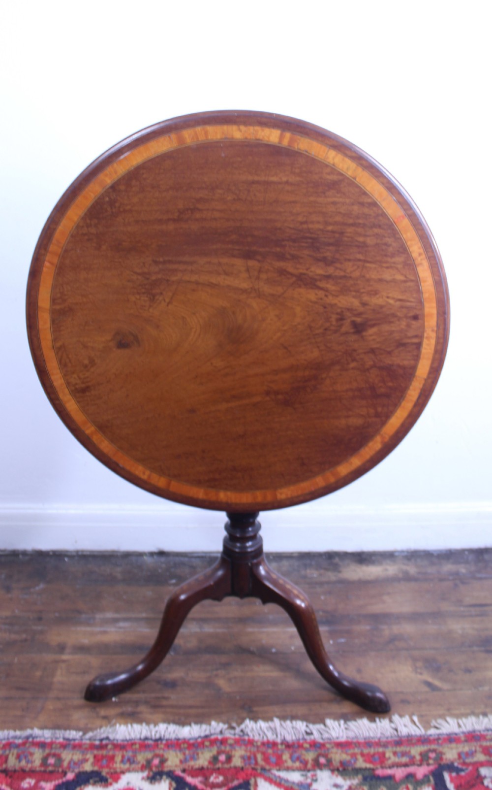 An 18th-century George III mahogany tilt-top tripod table with a circular crossbanded top tilted vertically on a turned stem and splayed legs. View XII