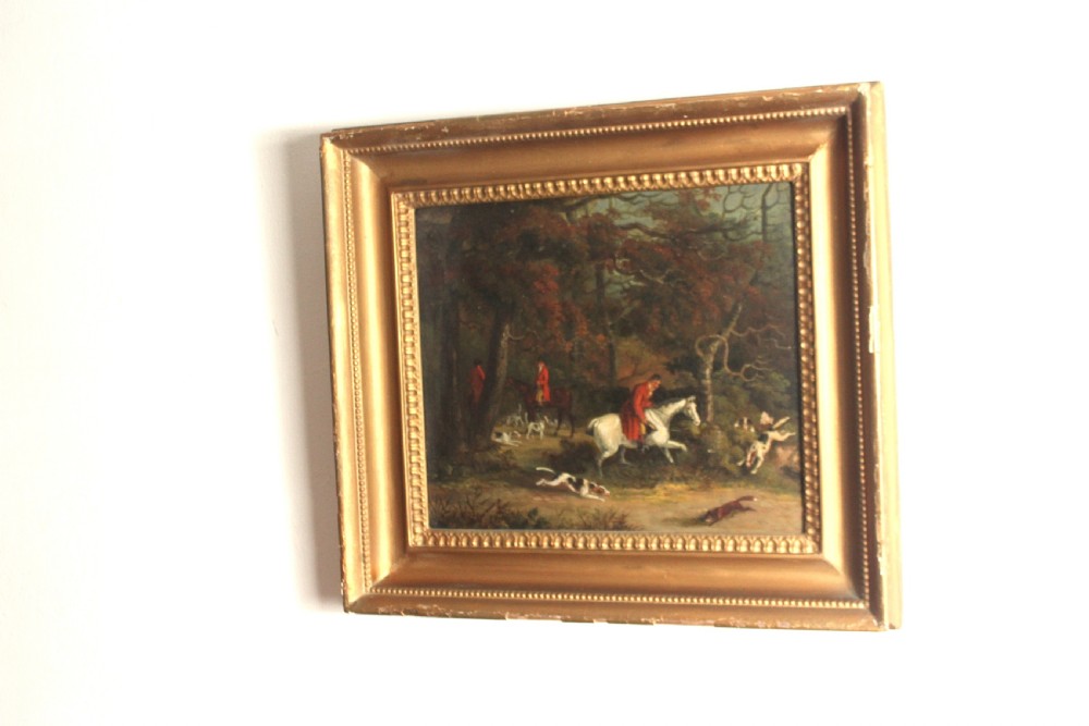 An early 19th-century oil painting depicting horse riders in red coats with hunting hounds pursuing a fox through a woodland, set in a gilded frame. View VI