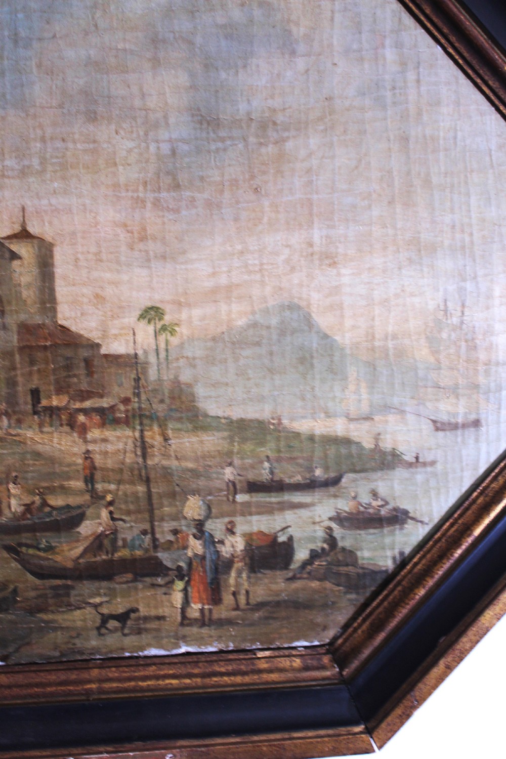 An octagonal framed early 19th-century oil painting depicting a Brazilian coastal landscape with colonial buildings, figures along the shore, and boats on the water. View III