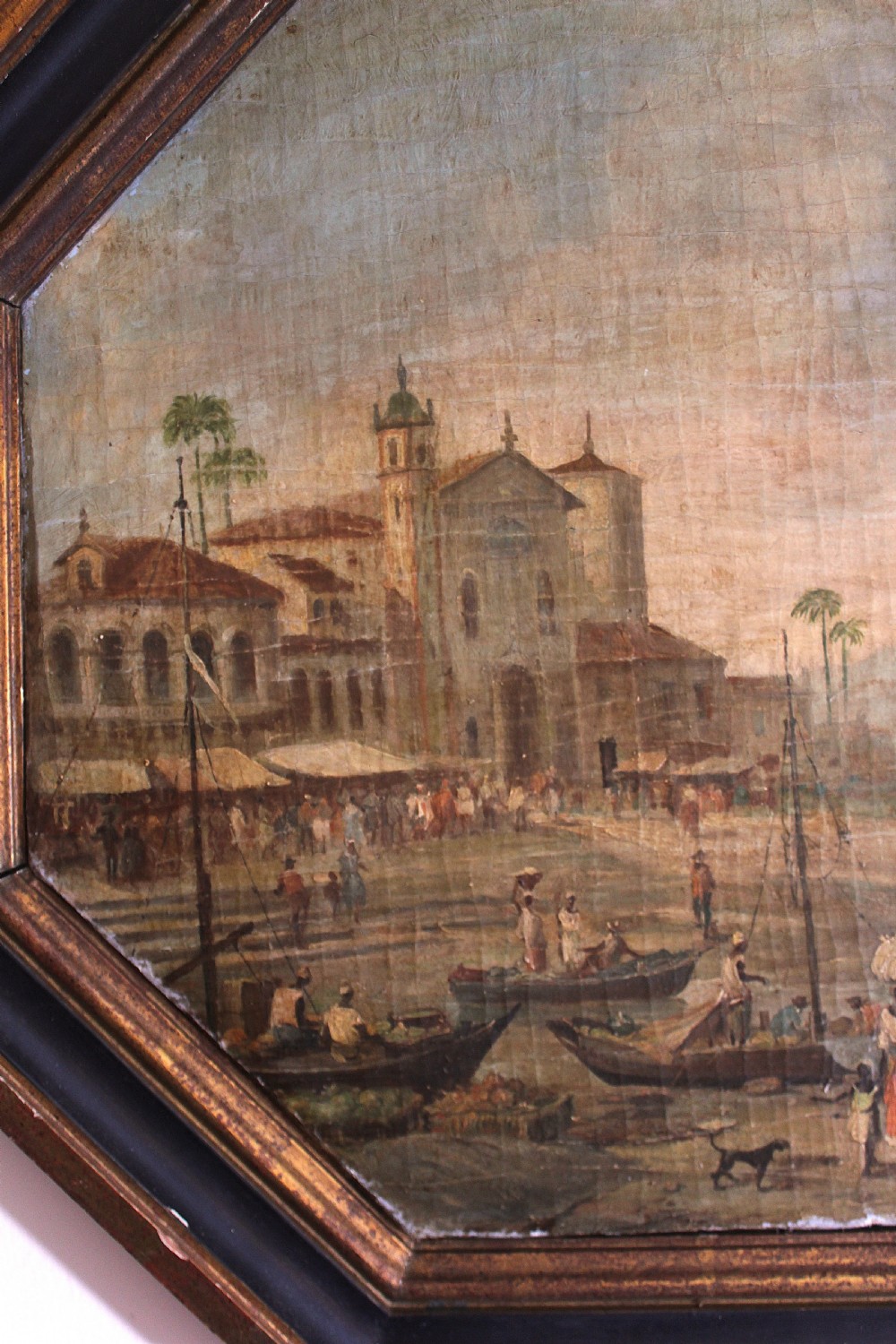 An octagonal framed early 19th-century oil painting depicting a Brazilian coastal landscape with colonial buildings, figures along the shore, and boats on the water. View V
