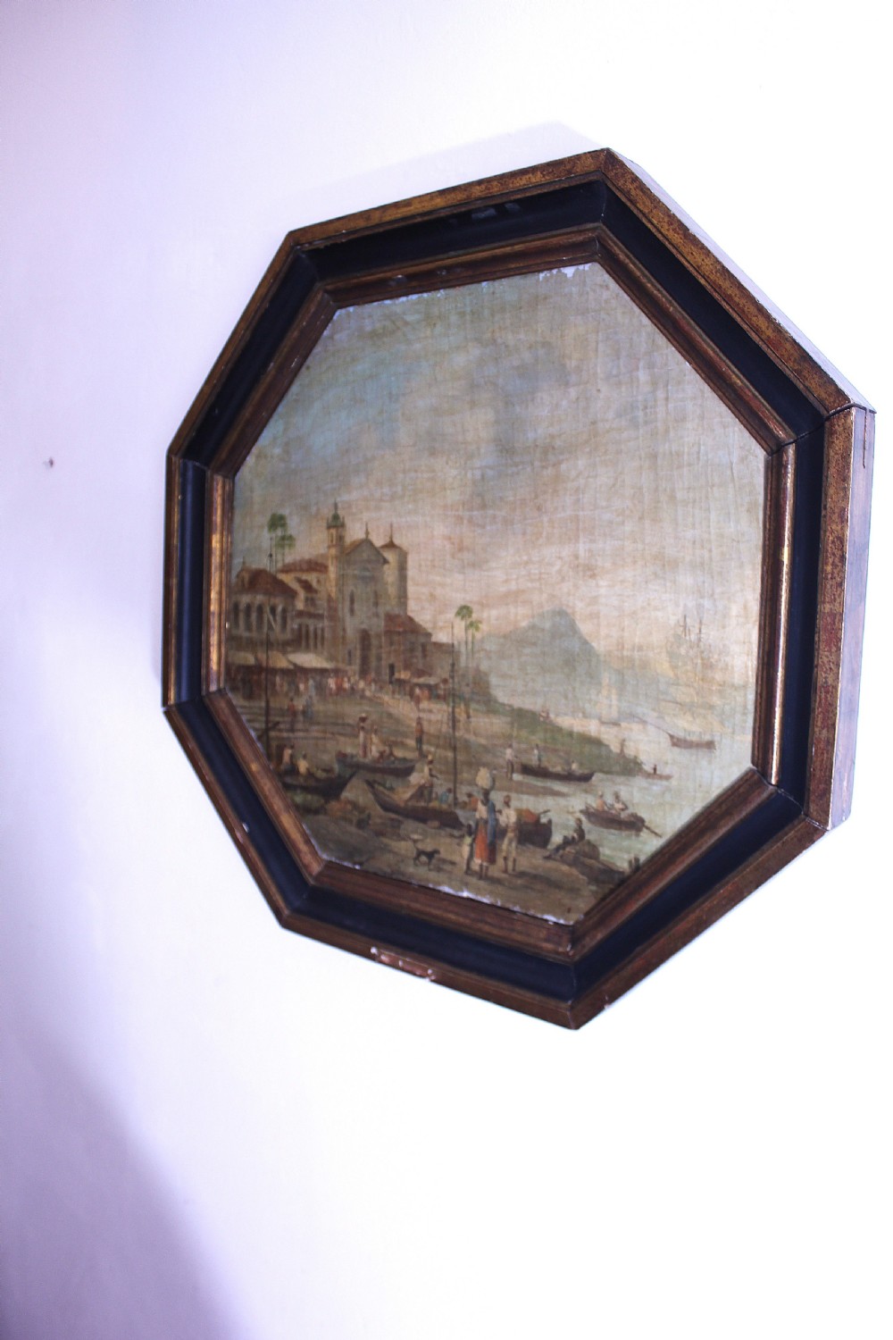 An octagonal framed early 19th-century oil painting depicting a Brazilian coastal landscape with colonial buildings, figures along the shore, and boats on the water. View XI