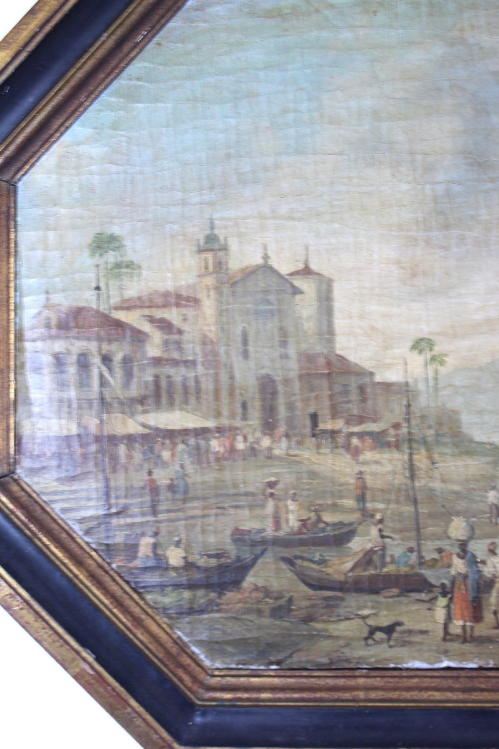 An octagonal framed early 19th-century oil painting depicting a Brazilian coastal landscape with colonial buildings, figures along the shore, and boats on the water. View XII