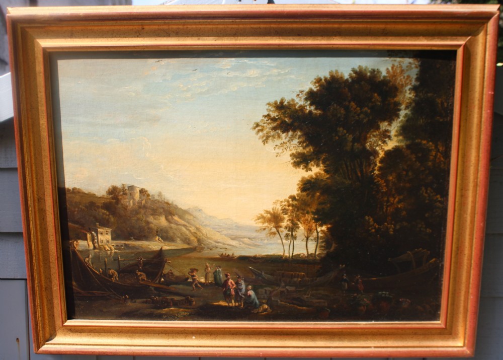 An 18th-century classical landscape oil painting depicting riverboats and figures beside a shore bathed in golden light, set within a gilded wooden frame.