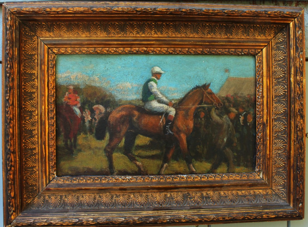 An early 20th-century impressionistic oil painting of a mounted jockey on a bay racehorse in a paddock, framed in a carved gilded wooden frame.