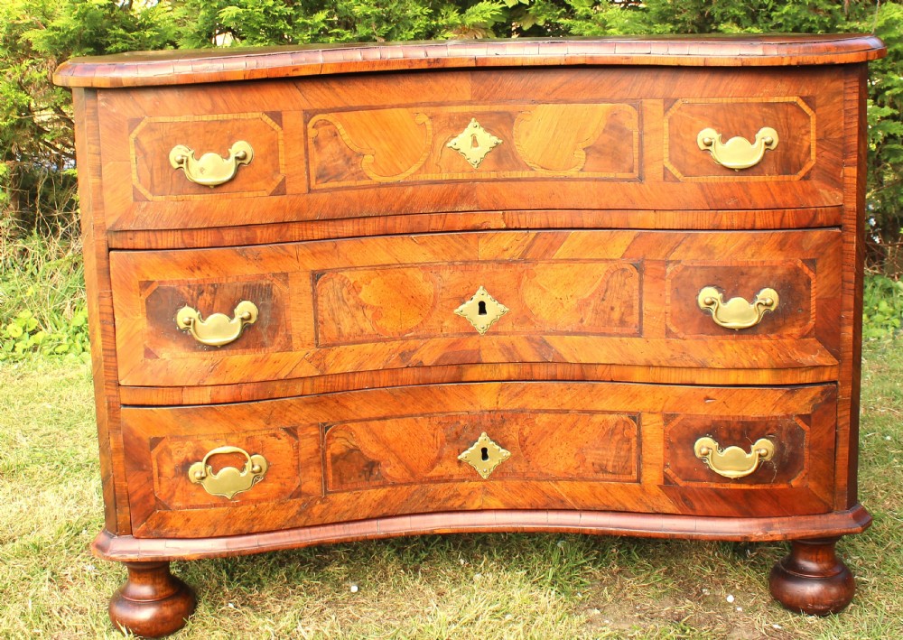 An eighteenth-century Austrian Baroque walnut chest of drawers featuring three serpentine drawers with marquetry inlay and brass handles on bun feet.