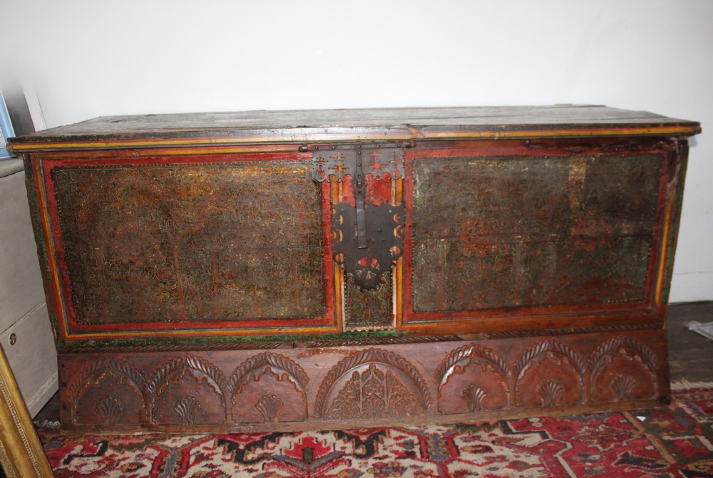 An antique Spanish painted blanket chest featuring ornate panels, a central wrought iron lockplate, and a carved arcaded base.