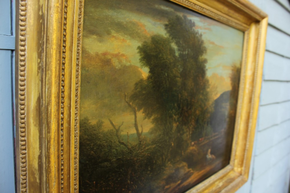 A 19th-century English pastoral oil painting depicting trees, hills, and figures beside a body of water in a moulded gilt frame. View V