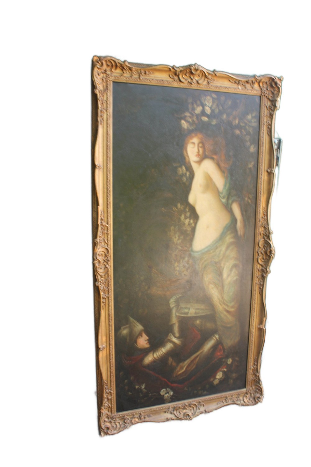 A large vertical Pre-Raphaelite oil painting depicting a knight in armour gazing up at a woman, set within an ornate carved gilt frame.