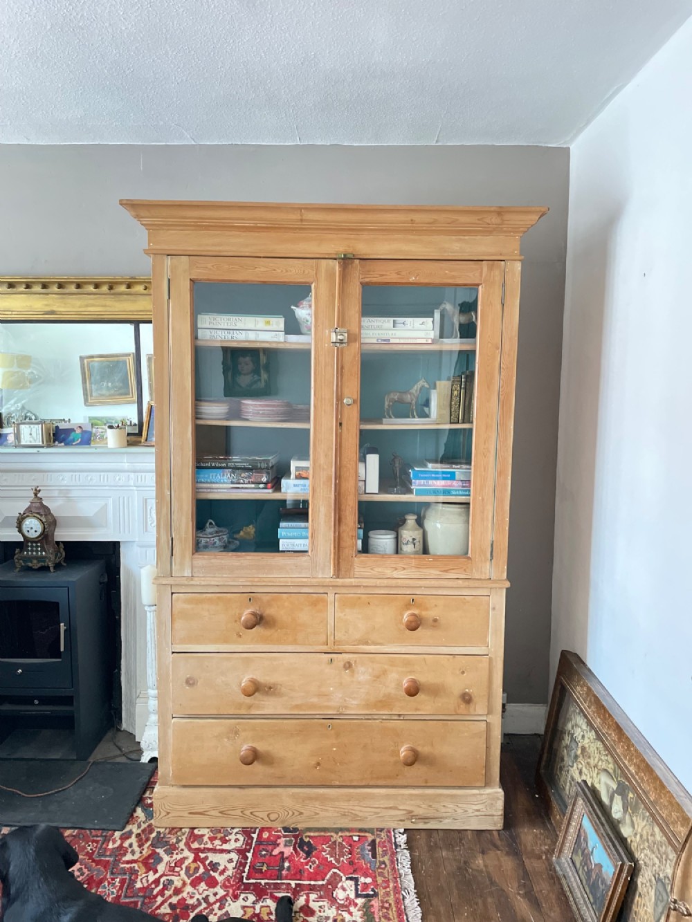 A Victorian waxed pine glazed bookcase featuring two upper glass cabinet doors with a blue painted interior over a chest of four drawers with turned knobs.