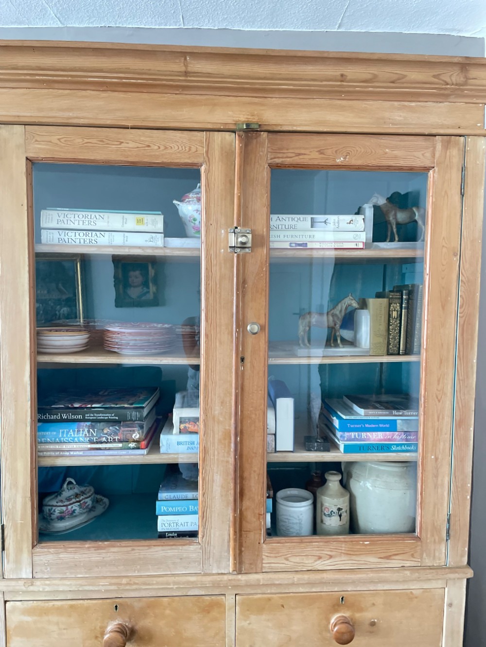 A Victorian waxed pine glazed bookcase featuring two upper glass cabinet doors with a blue painted interior over a chest of four drawers with turned knobs. View II