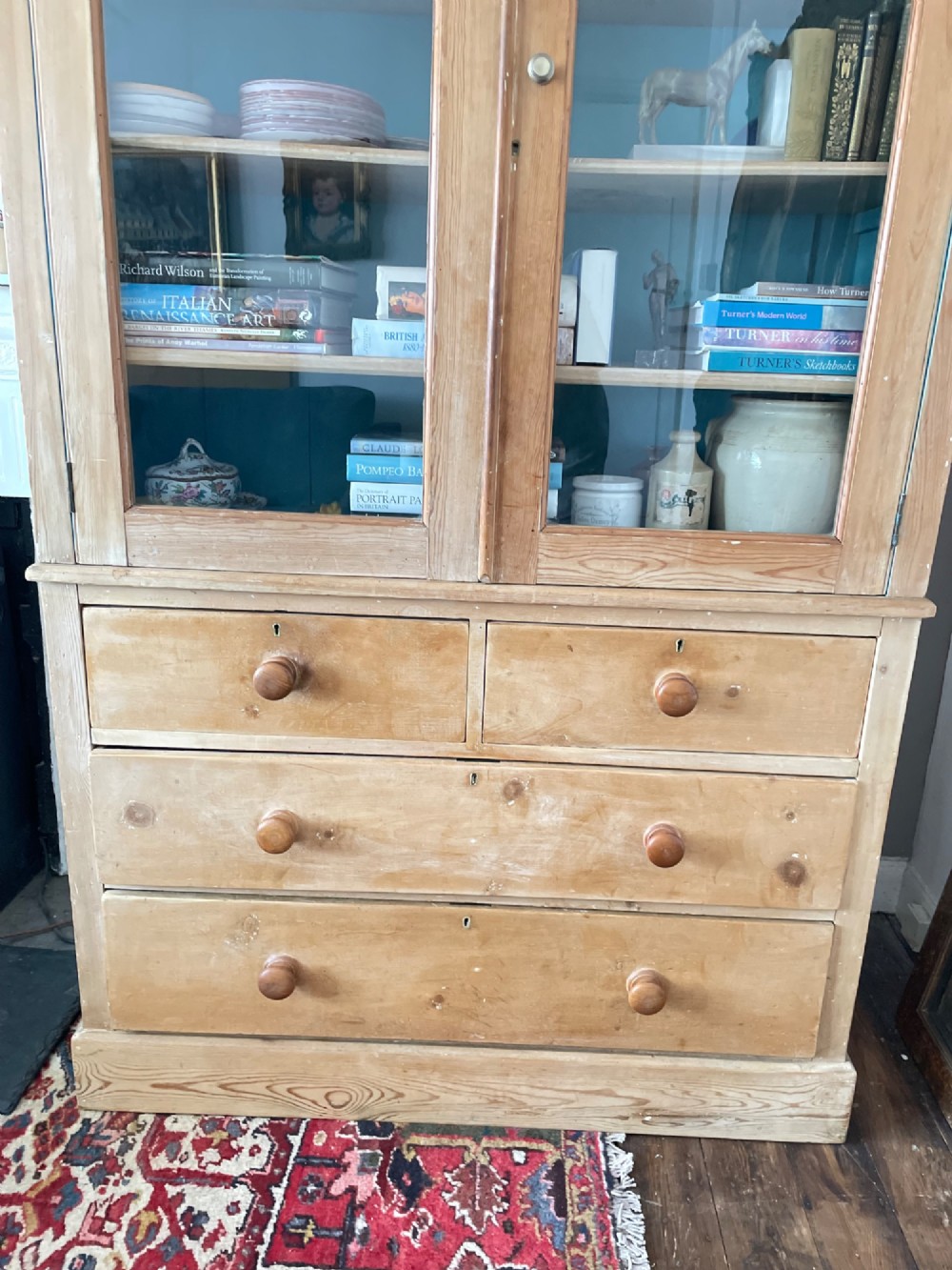 A Victorian waxed pine glazed bookcase featuring two upper glass cabinet doors with a blue painted interior over a chest of four drawers with turned knobs. View III
