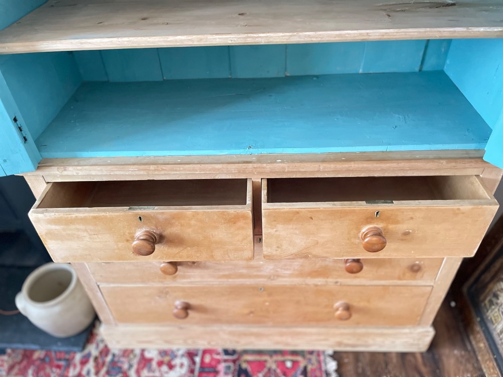 A Victorian waxed pine glazed bookcase featuring two upper glass cabinet doors with a blue painted interior over a chest of four drawers with turned knobs. View V