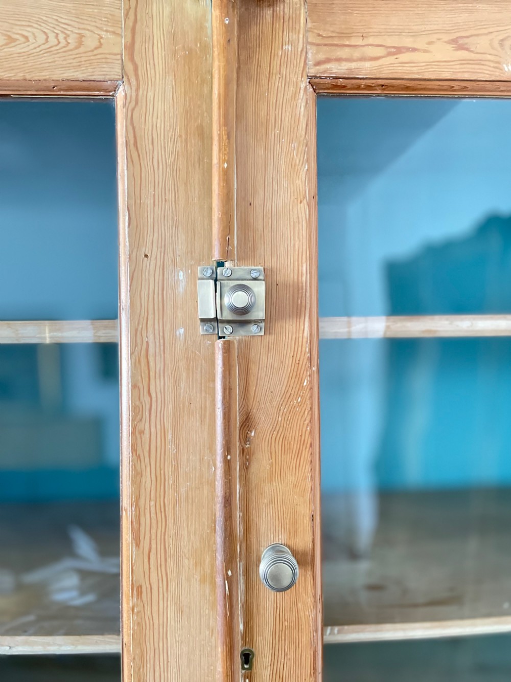 A Victorian waxed pine glazed bookcase featuring two upper glass cabinet doors with a blue painted interior over a chest of four drawers with turned knobs. View VIII
