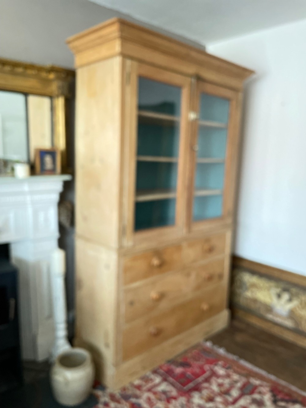 A Victorian waxed pine glazed bookcase featuring two upper glass cabinet doors with a blue painted interior over a chest of four drawers with turned knobs. View IX