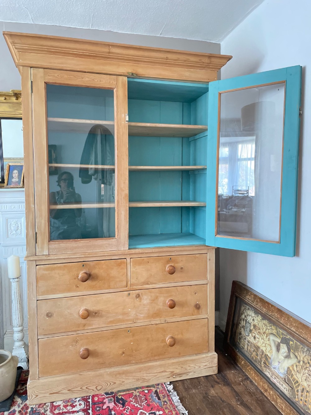 A Victorian waxed pine glazed bookcase featuring two upper glass cabinet doors with a blue painted interior over a chest of four drawers with turned knobs. View XII