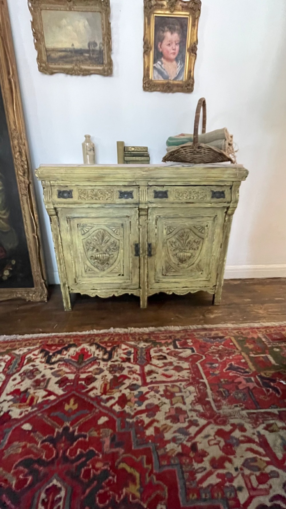 An antique French provincial sideboard featuring distressed yellow painted wood, two carved panel doors with urn motifs, two upper drawers, and a pink marble top surface. View VI