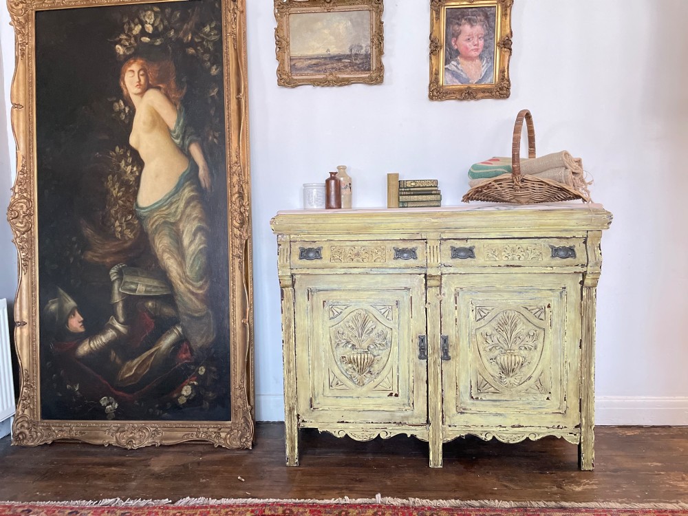 An antique French provincial sideboard featuring distressed yellow painted wood, two carved panel doors with urn motifs, two upper drawers, and a pink marble top surface. View VII