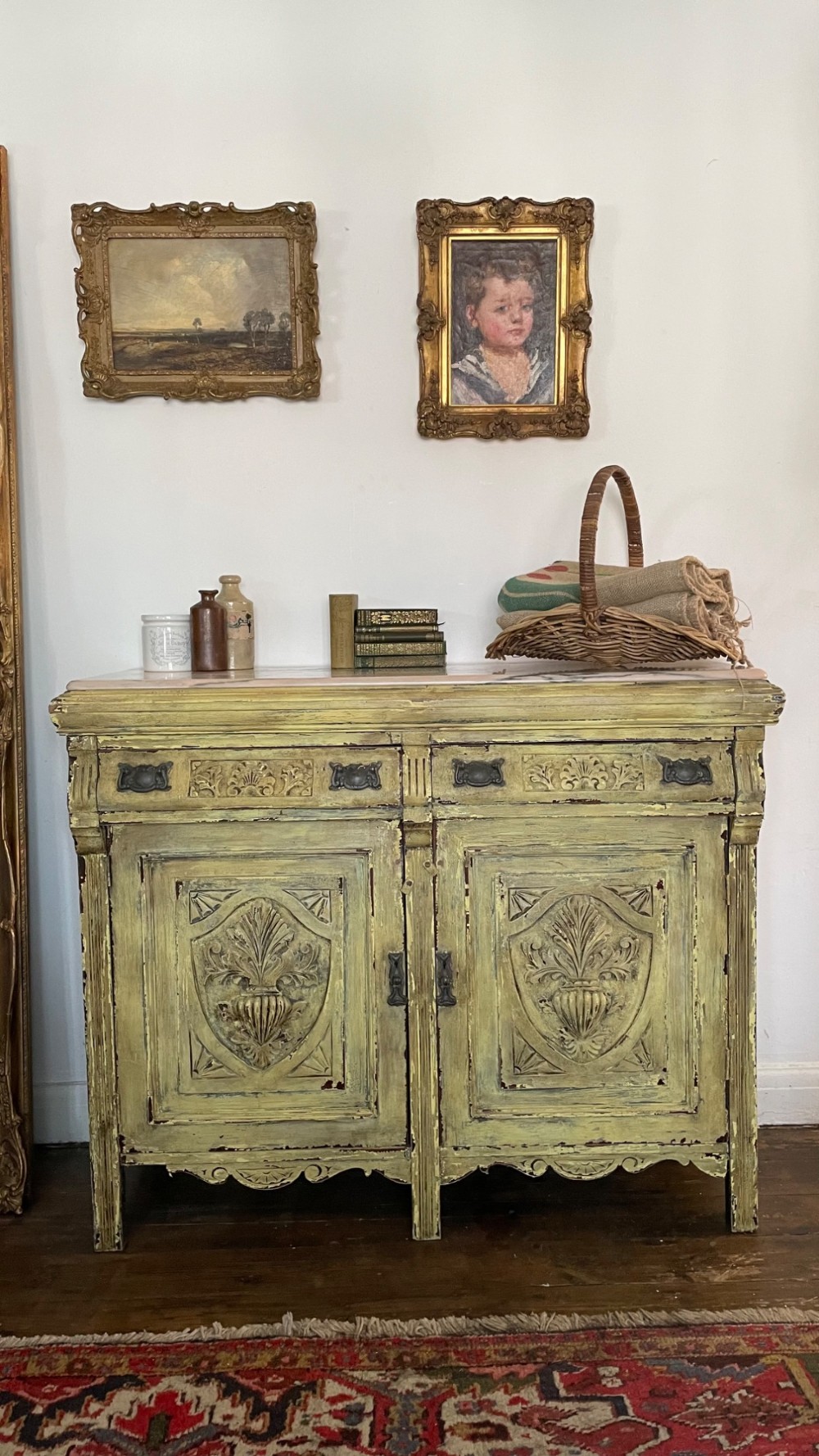 An antique French provincial sideboard featuring distressed yellow painted wood, two carved panel doors with urn motifs, two upper drawers, and a pink marble top surface. View VIII