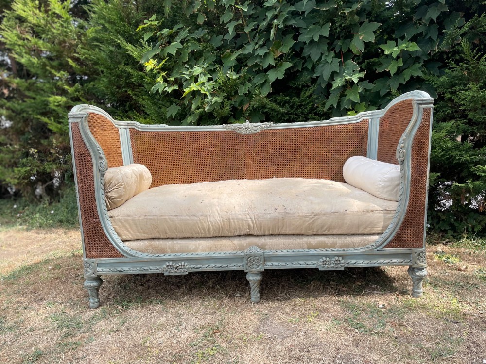 A French Louis XVI style daybed featuring a grey-painted curved timber frame with woven cane panels, fitted with a cream linen mattress cushion and two bolster pillows. View II
